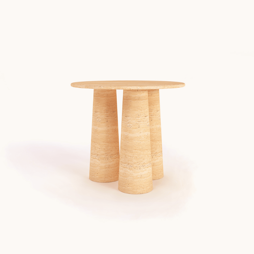 The Elysian Triple Cone Travertine Round Table by Travertable features a natural stone finish with three cylindrical legs. Its smooth surface and light beige color add elegance, set against a plain white background.