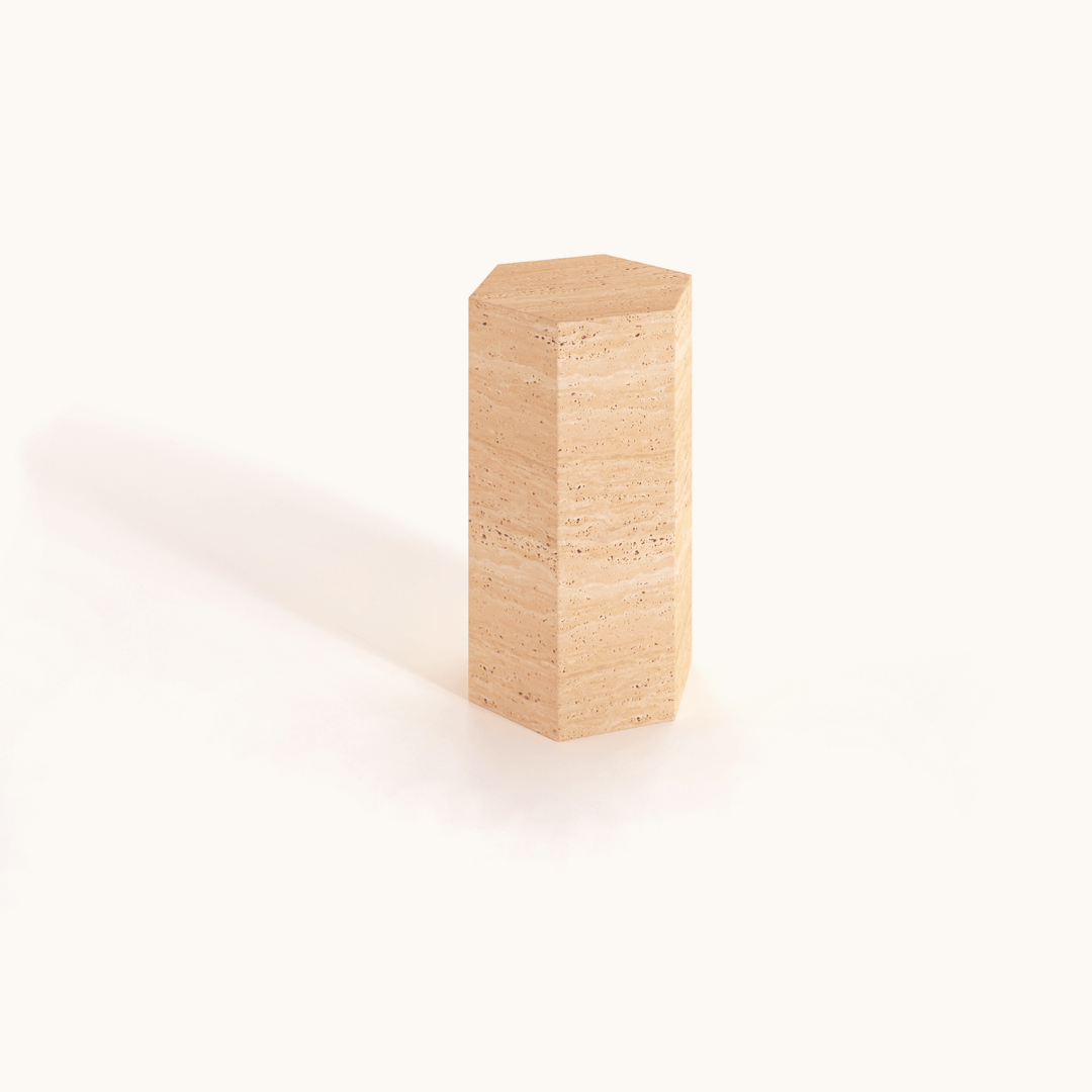 Travertables Geometric Travertine Pedestal features a unique beige hexagonal stone block design, standing upright on a light background and casting a soft left shadow. Its natural textured patterns enhance its earthy appeal and architectural elegance.