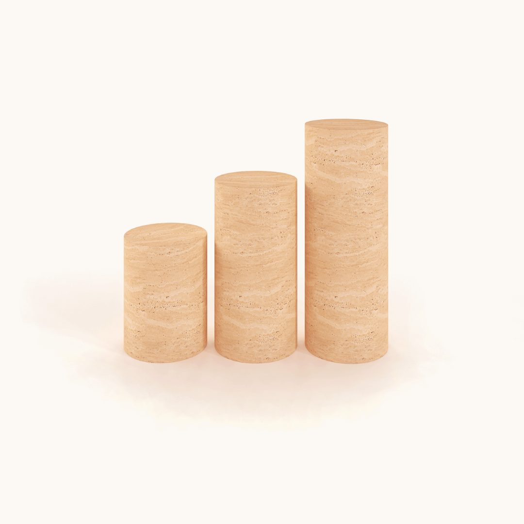 Three Travertable cylindrical pedestals, resembling travertine stones, are arranged on a white background in a staircase-like progression. The visible wood grain of these Travertine Pedestal side tables adds natural texture, creating an earthy and sophisticated look.