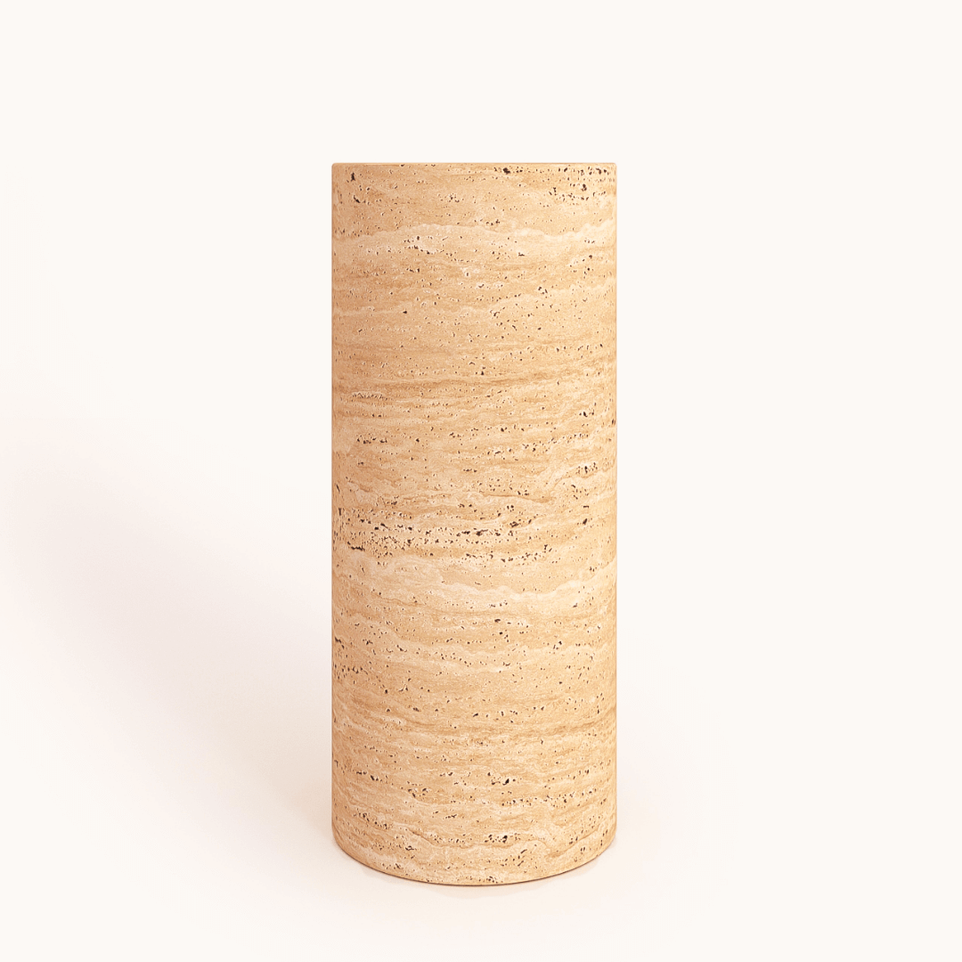 The Travertable Travertine Pedestal is a minimalist side table made of natural travertine stone, featuring a cylindrical shape, tan color, and horizontal striations against a plain white background.