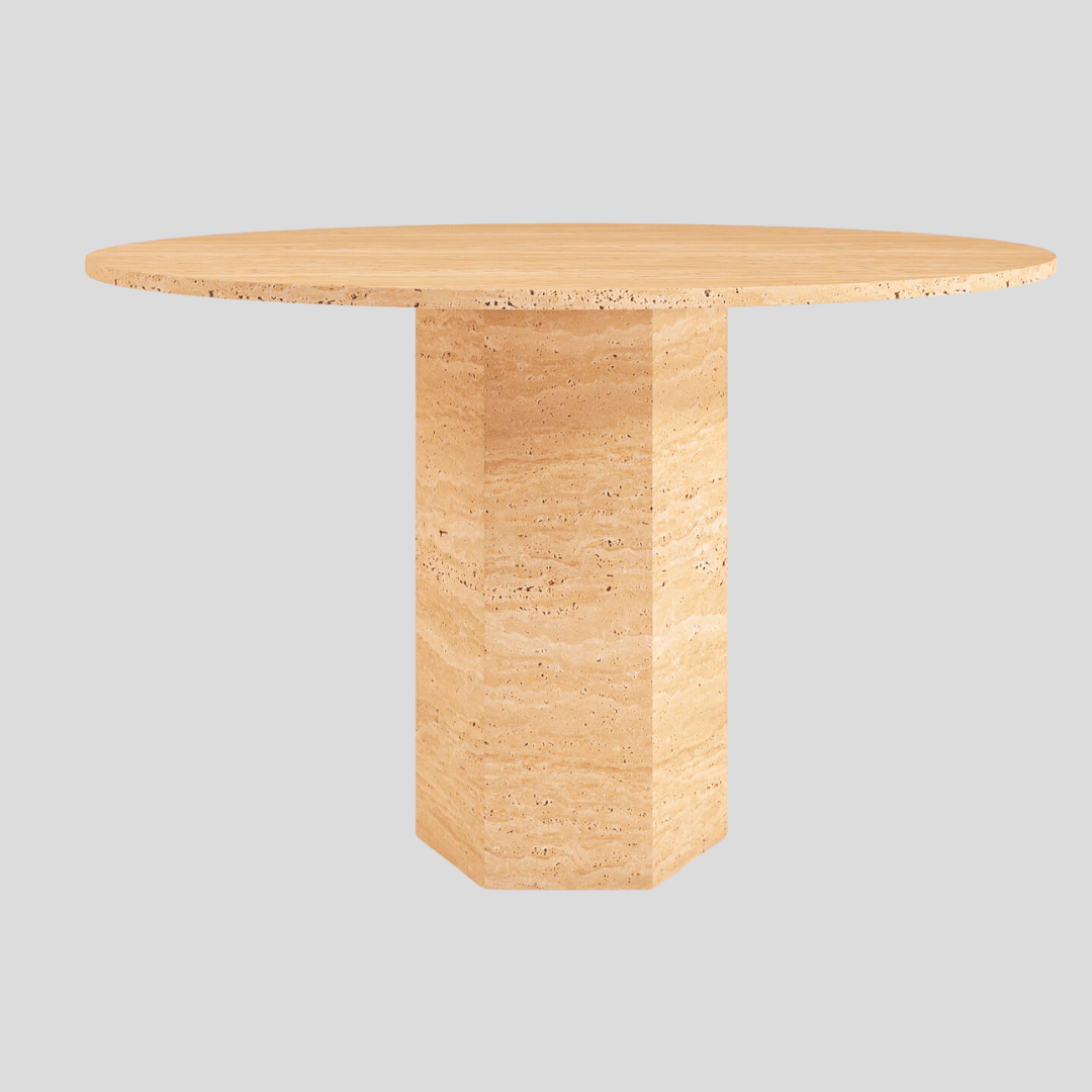 The Travertable Hexagon Round Travertine Dining Table features a round beige marble top on a solid hexagonal travertine base, set against a plain gray backdrop.