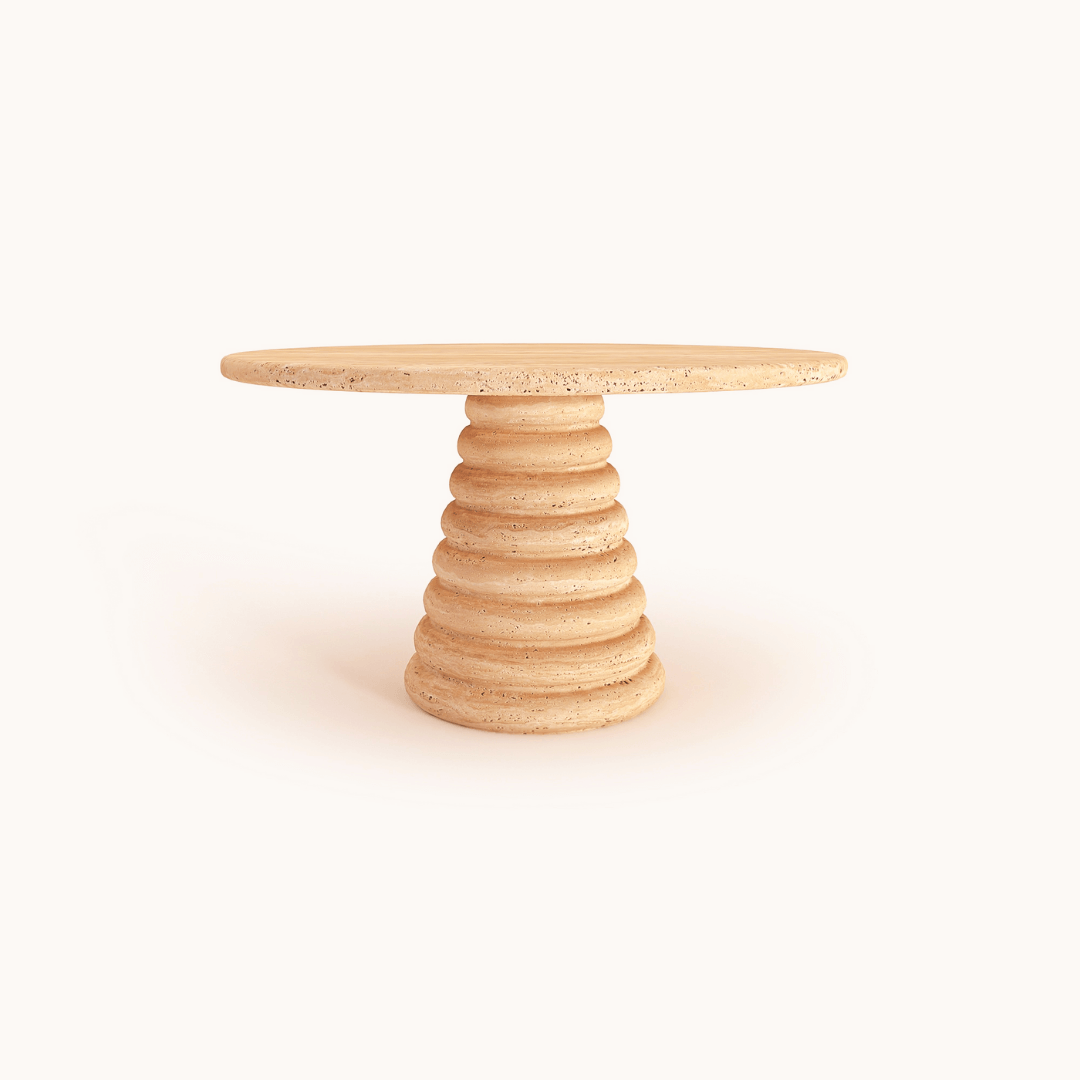 The Travertable Designer Coffee Table features a round, beige travertine tabletop with a grooved, tapered cylindrical base designed like stacked discs. This durable piece showcases natural beauty against a plain, light background, embodying sculptural stone aesthetics as an elegant statement piece.
