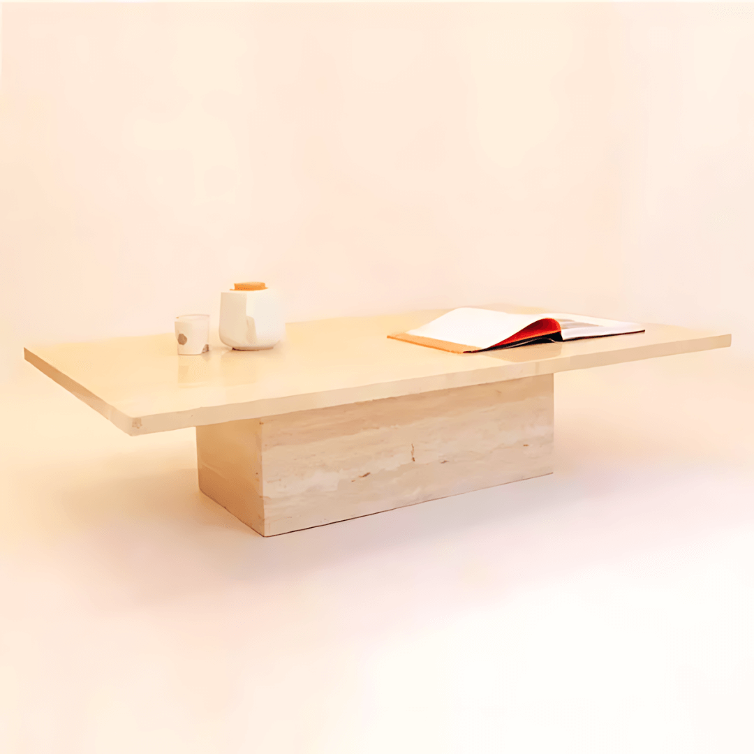The Minimalist Travertine Accent Coffee Table by Travertable, featuring a thick rectangular base, elegantly supports an open book, a white cup, and a teapot. Its simple design against a soft neutral backdrop enhances luxury home decor.