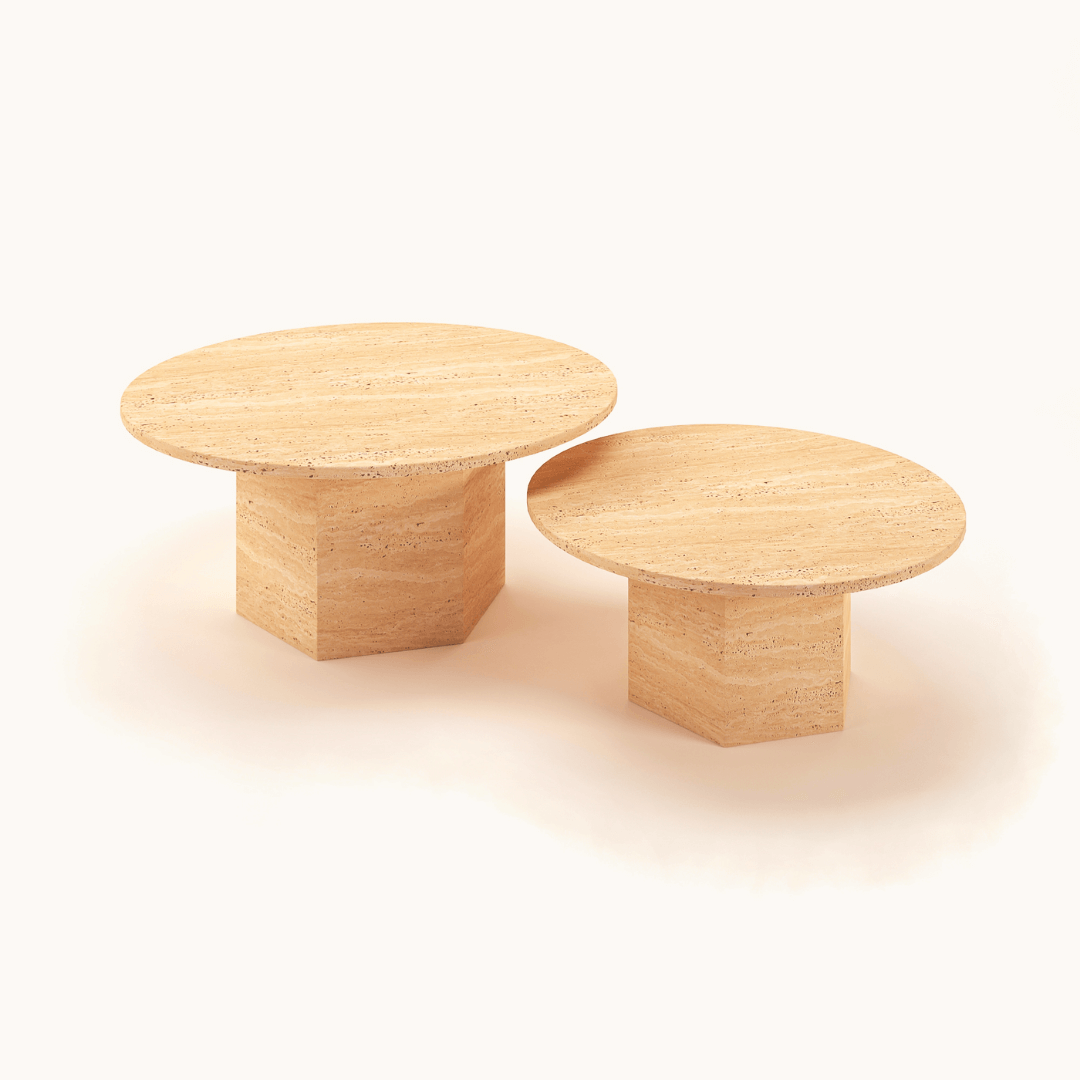 Set against a plain backdrop, two wooden tables showcase a timeless design with round tops and sturdy rectangle bases. The elegance of the Desert Serenity Travertine Coffee Table by Travertable is highlighted as the smaller piece sits gracefully in front of its larger counterpart.