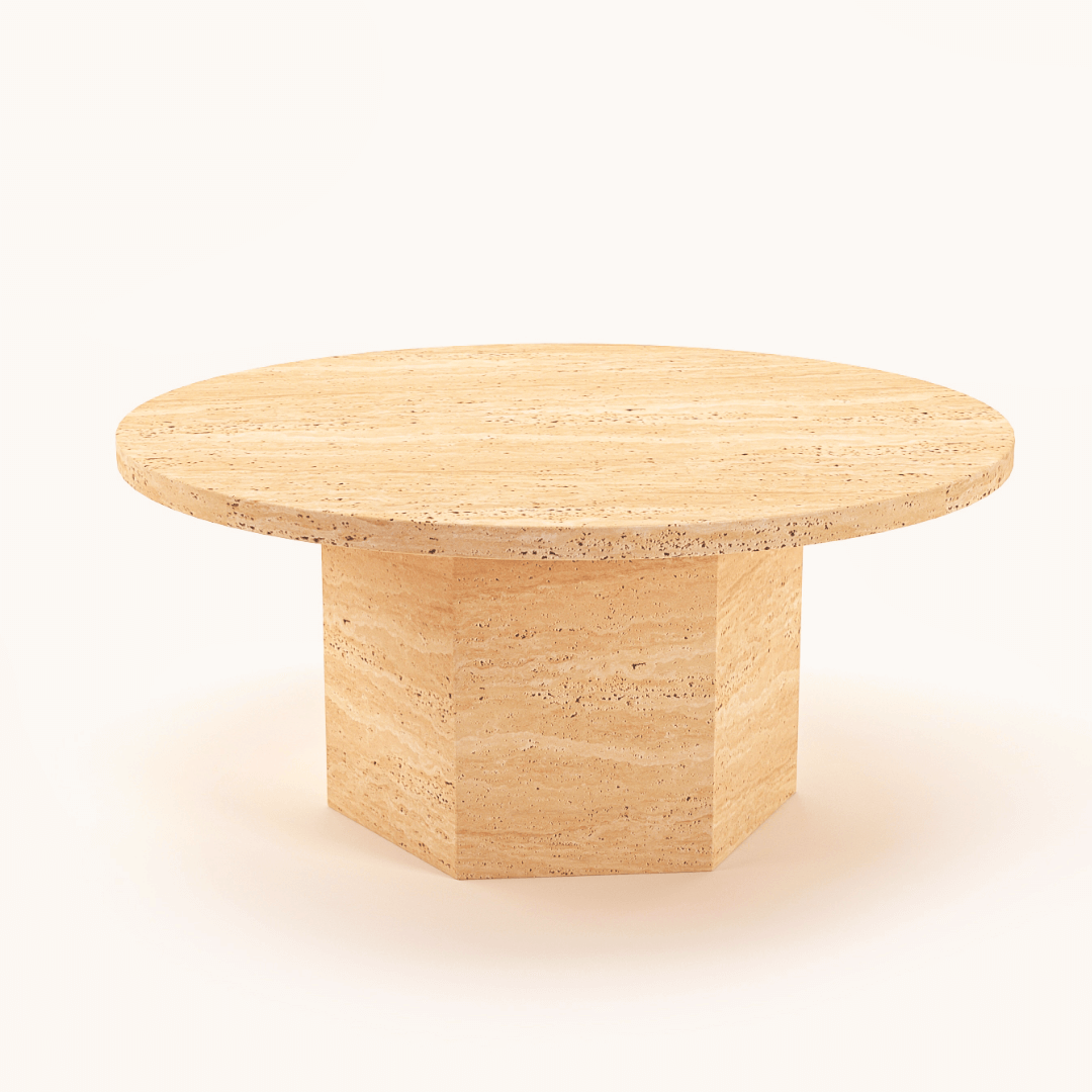 The Desert Serenity Coffee Table by Travertable features a smooth round travertine top and a thick hexagonal pedestal, offering an earthy, sculptural design with a soft honed finish, set against a plain white background.