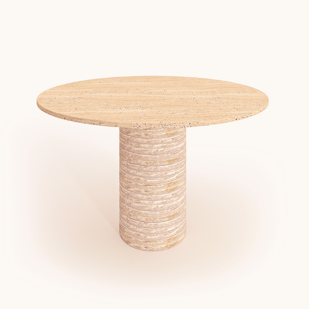 The Rustic Round Travertine Dining Table by Travertable features a customizable wooden tabletop with a smooth finish, supported by a single cylindrical pedestal. It boasts a light wood grain texture reminiscent of rustic travertine against a plain beige background.