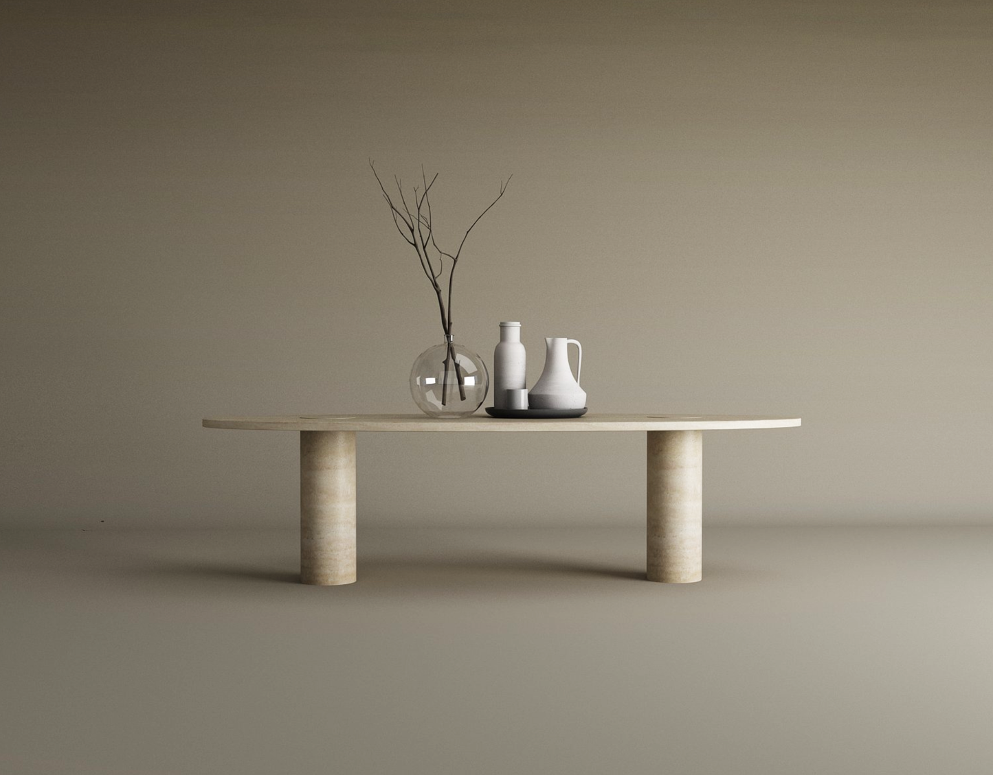 The TRAVERTABLE Ellipse Travertine Coffee Table with Solid Cylindrical Base showcases natural veining and supports a clear glass vase with branches, a white vase, and a white pitcher on a black dish, set against a plain beige background.
