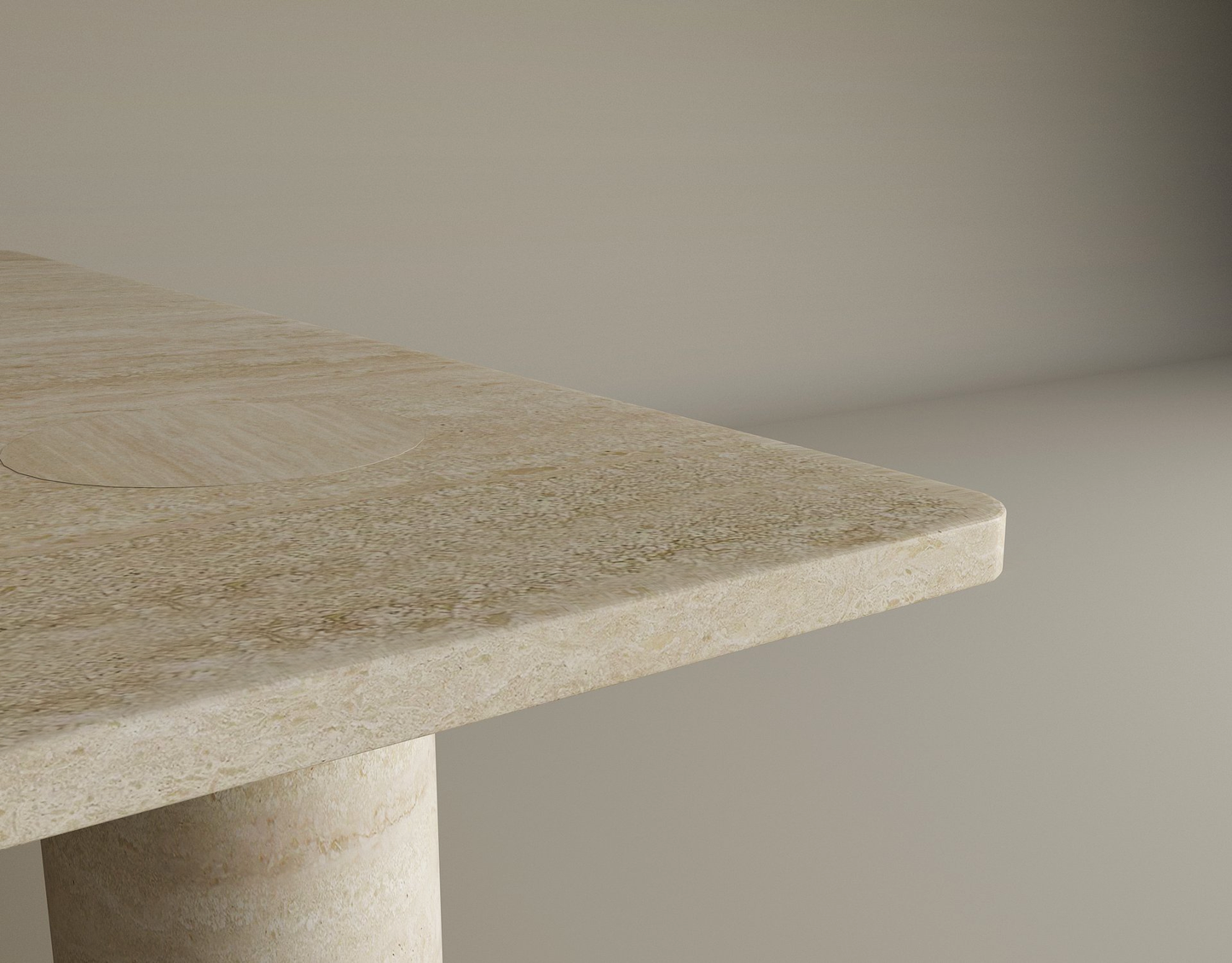 A close-up shows the corner of TRAVERTABLE’s Rectangular Travertine Coffee Table, featuring warm beige travertine, a solid cylindrical base, and rounded edge, set against a plain light background. Customizable to your space.
