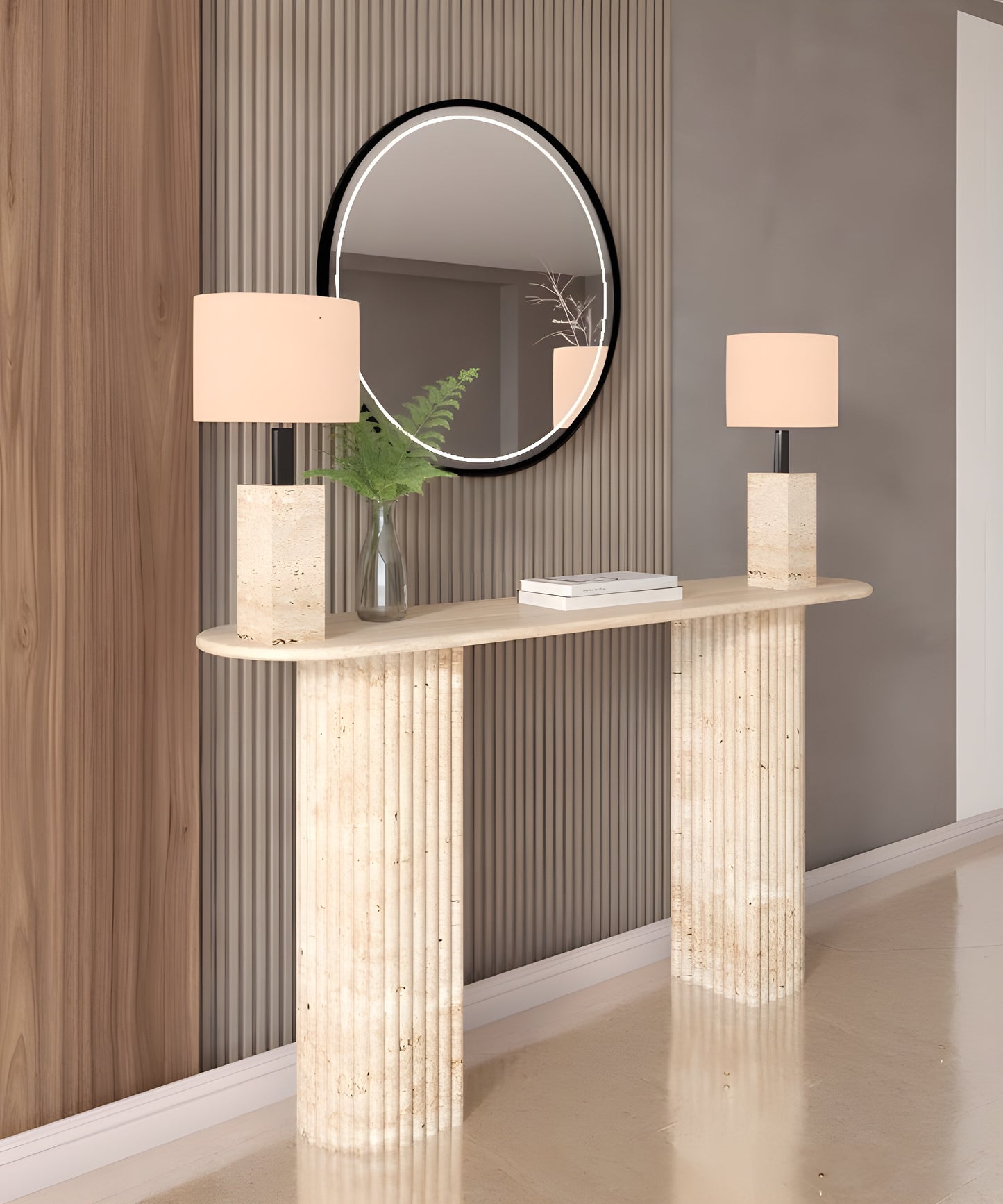 A TRAVERTABLE Ovale Travertine Console Table with a fluted round solid stone base holds two square lamps and a glass vase with green fern leaves. Above, a black-framed round mirror complements the vertical wood panels and classic style.