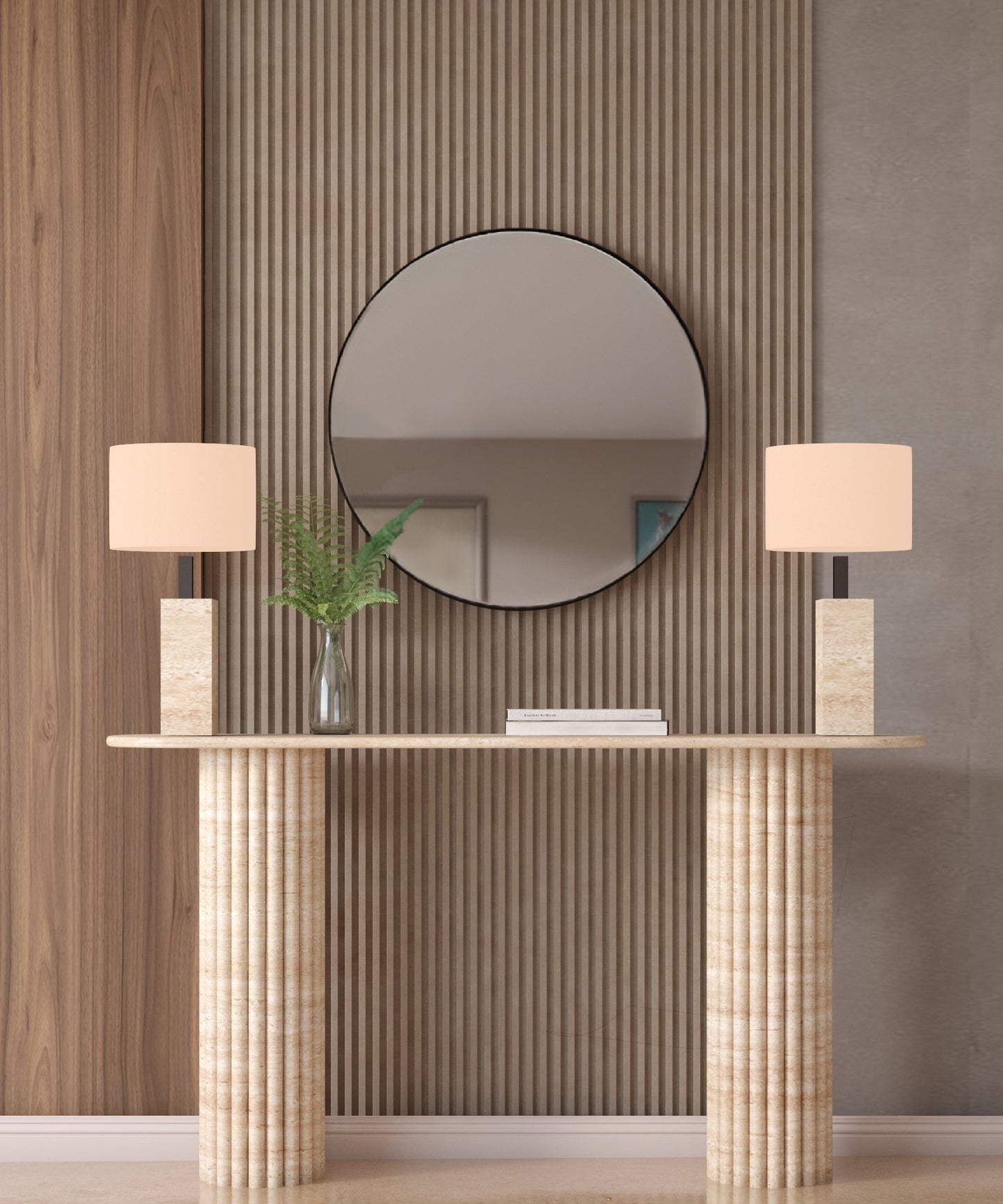 The Ovale Travertine Console Table by TRAVERTABLE features a vertical groove organic stone base and is customizable. Styled here with beige lamps, a glass vase with green leaves, and a round mirror on a wood slat accent wall behind it.