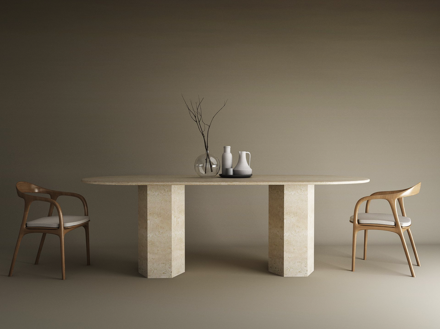 A minimal dining setup features the TRAVERTABLE Oval Travertine Dining Table with a hexagonal stone base, two wooden chairs with white cushions, three ceramic vessels, and a glass vase with branches, all set against a plain brown background.