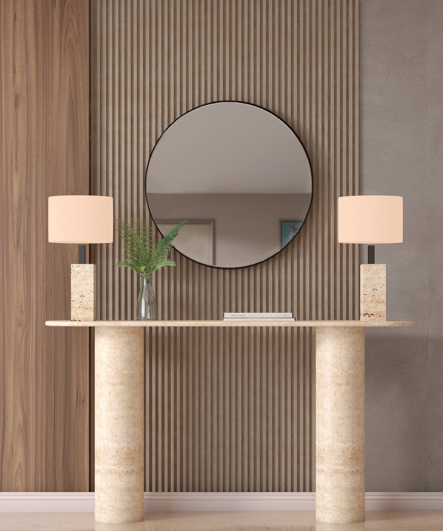 A round mirror hangs above the TRAVERTABLE Ovale Travertine Console Table with a smooth pure stone base, flanked by two stone lamps and a vase of green fern leaves against neutral vertical wood and textured panels.