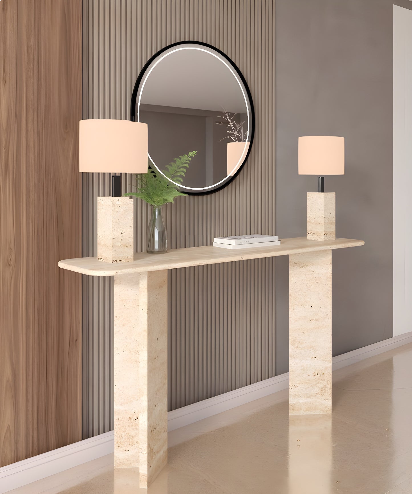 The TRAVERTABLE Rectangular Travertine Console Table with Split-V Pedestal Base displays two matching lamps, a clear vase with green foliage, and a round mirror above, all set against vertically paneled walls.