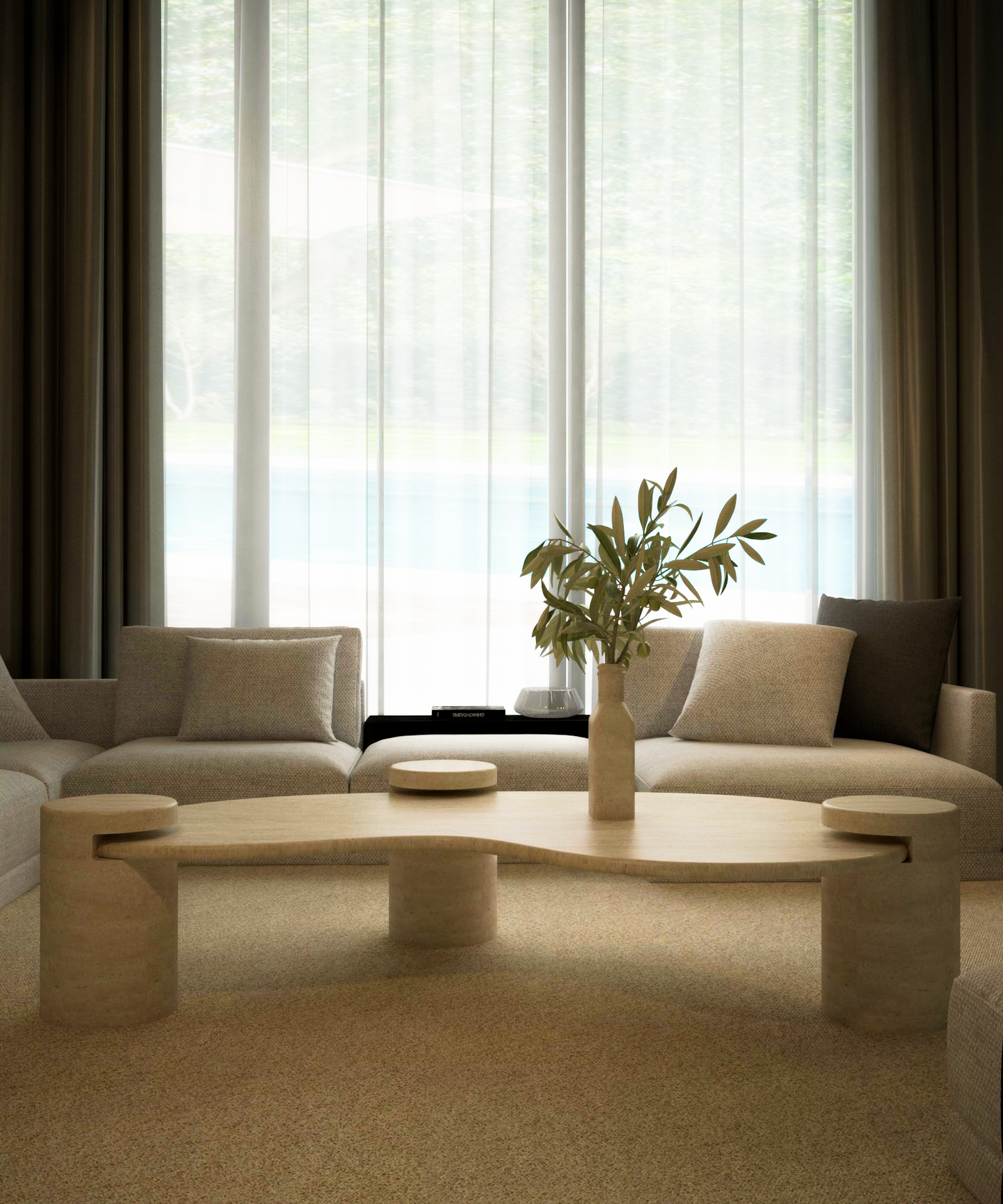 A modern living room features cream sofas, grey cushions, and the TRAVERTABLE Wavy Travertine Coffee Table with Cylindrical Base – Organic Flow, topped with a ceramic vase of leafy branches. Sheer curtains on tall windows let in soft light and reveal lush greenery outside.