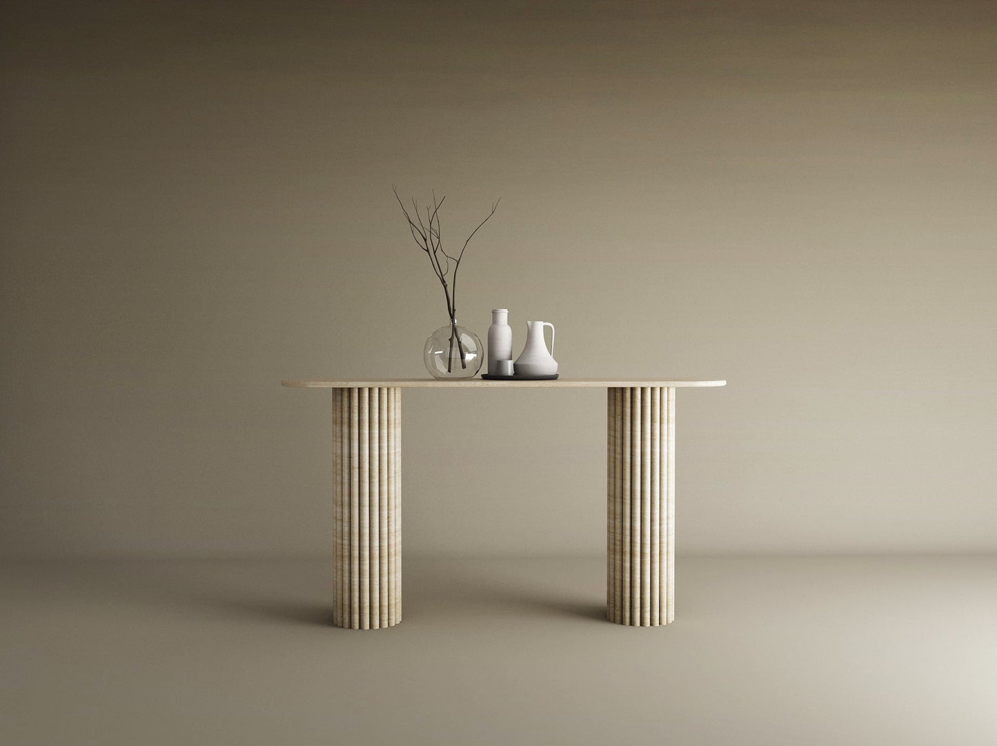 A TRAVERTABLE Ovale Travertine Console Table with Vertical Groove Base stands against a beige wall, topped with three vases—clear, white, off-white—and bare branches, creating a sculptural centerpiece in this minimal scene.