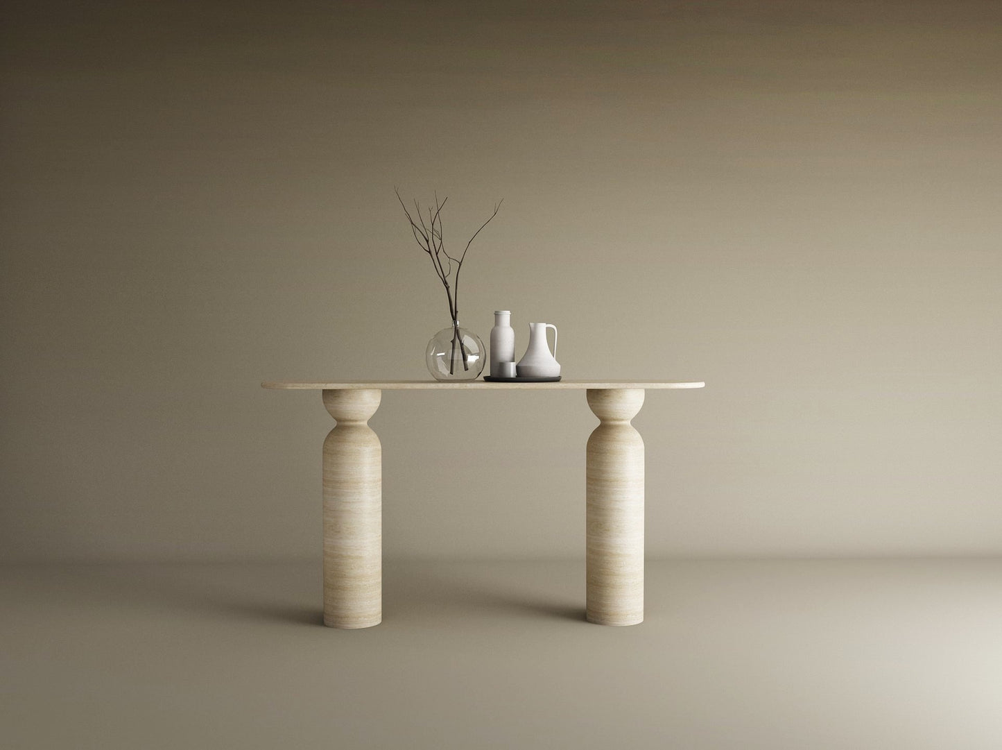 The Ovale Travertine Console Table by TRAVERTABLE, featuring a sculptural round base in organic travertine stone, displays a thin branch in a glass vase, a white pitcher, and jug against a beige backdrop—an understated statement piece.