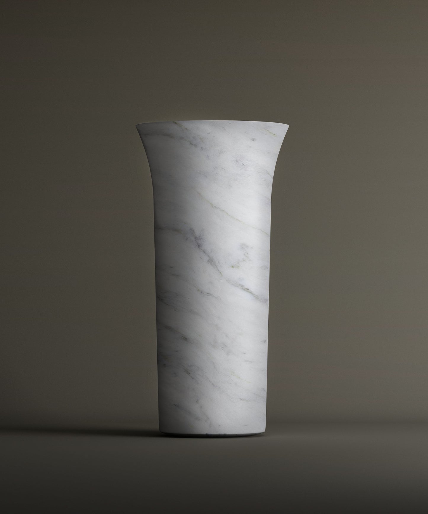 The TRAVERTABLE Carrara Marble Cylinder Pedestal Vanity Sink, with a tall cylindrical shape, white marble finish, and subtle gray veining, stands upright against a plain background. It features a slightly flared rim for added elegance.