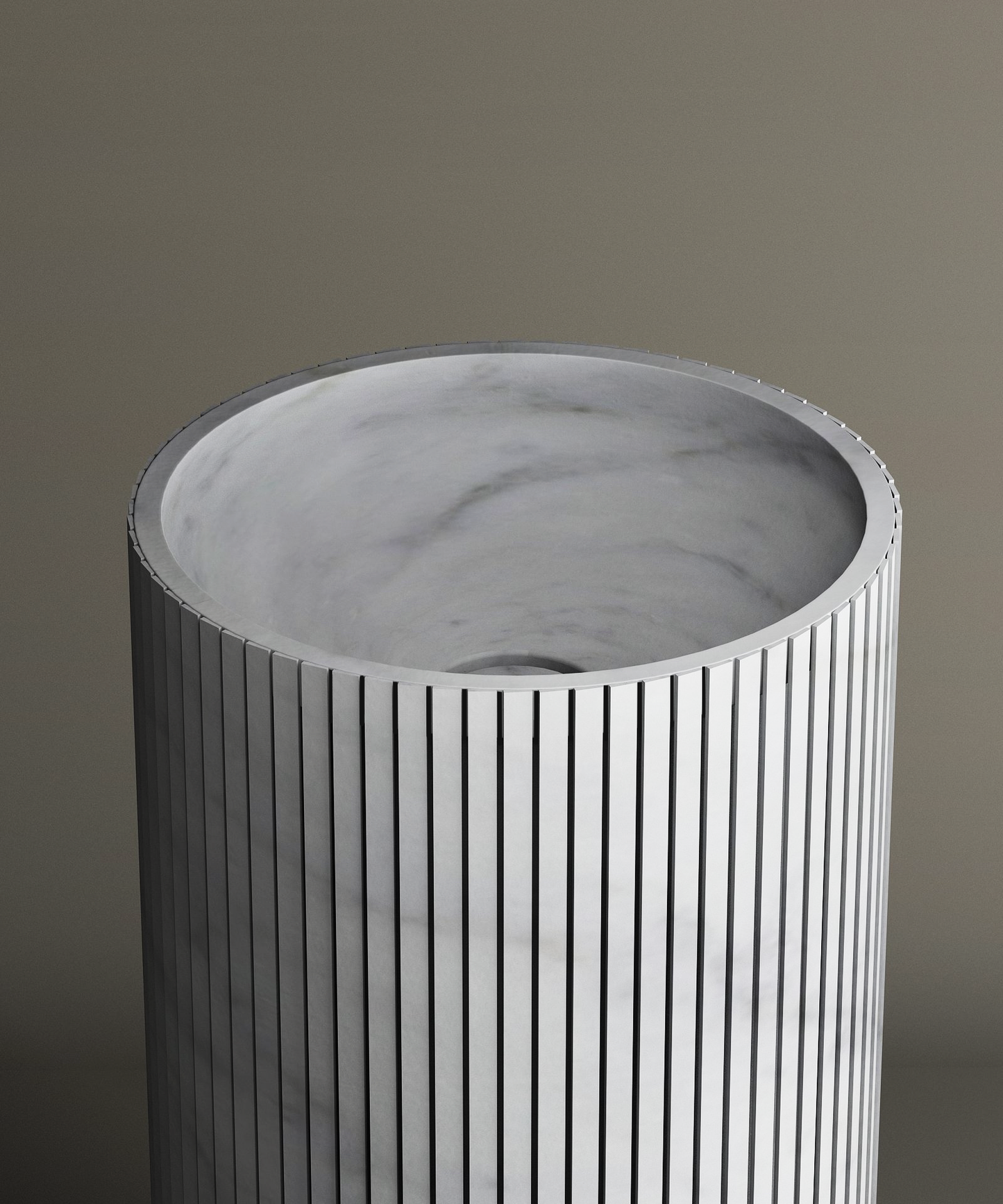 The TRAVERTABLE Carrara Round Fluted Marble Pedestal Vanity Sink features a cylindrical, fluted design with a marble texture and an open top revealing a smooth light gray interior, all set against a neutral background.