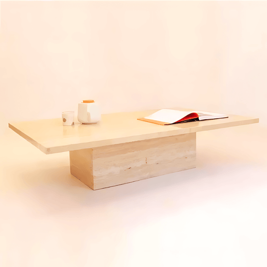The Minimalist Travertine Accent Coffee Table by Travertable, featuring a thick rectangular base, elegantly supports an open book, a white cup, and a teapot. Its simple design against a soft neutral backdrop enhances luxury home decor.