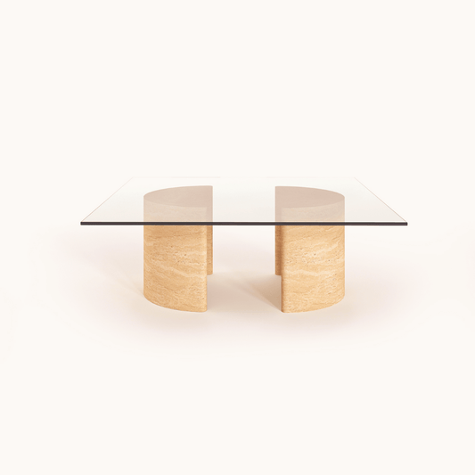 Introducing the Travertable Stone Horizon Coffee Table, a hand-sculpted masterpiece. This modern piece has a transparent glass top supported by dual semi-cylindrical beige stone bases, exuding natural beauty against its plain white background. Perfect for both modern and rustic interiors.
