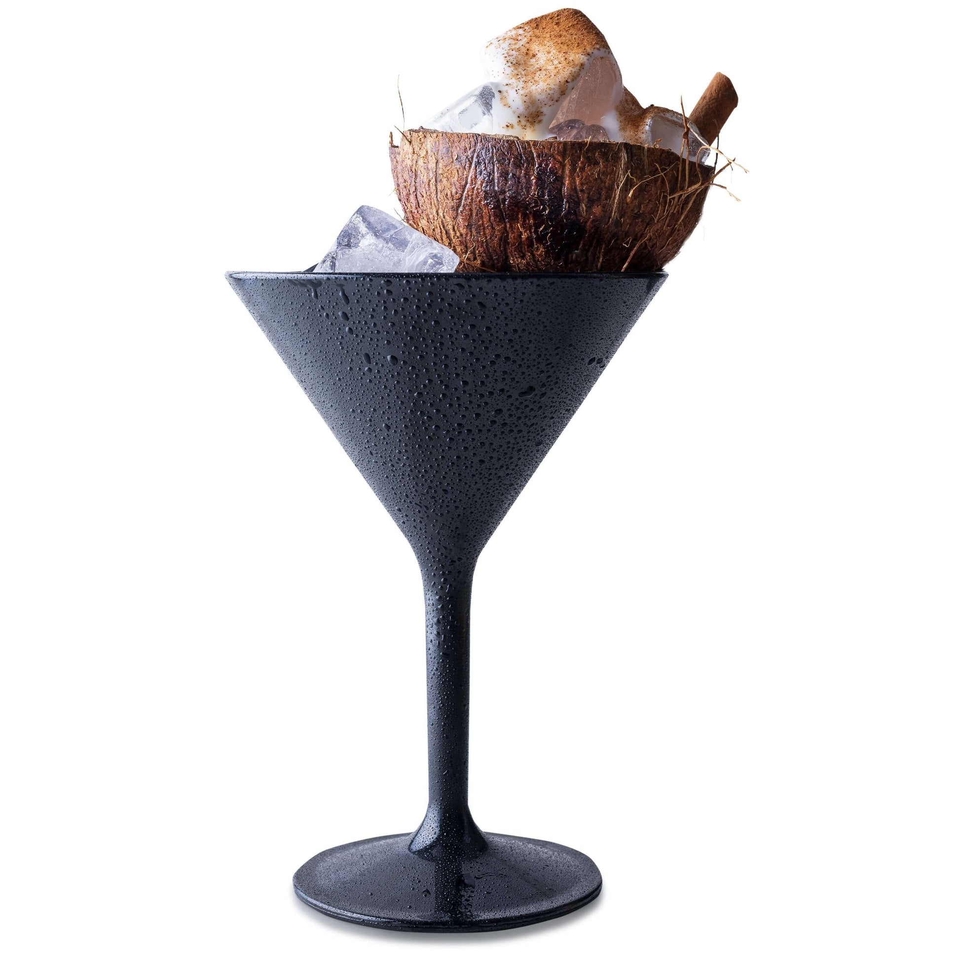 A Mamaco Home black Large Martini Glass, made from shatterproof polycarbonate, holds ice cubes topped with a coconut shell filled with more ice and crowned by a cinnamon stick, while glistening with condensation.