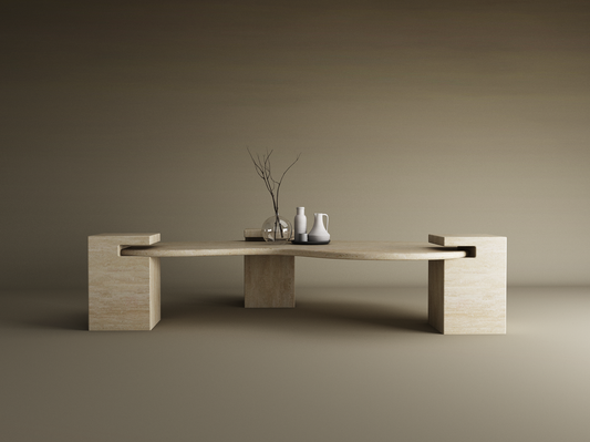 The Wavy Travertine Coffee Table with Square Base by TRAVERTABLE features a modern, sculptural form, shown here holding a clear glass vase with bare twigs and two ceramic pitchers (white and gray), set against a neutral gradient background with soft lighting.