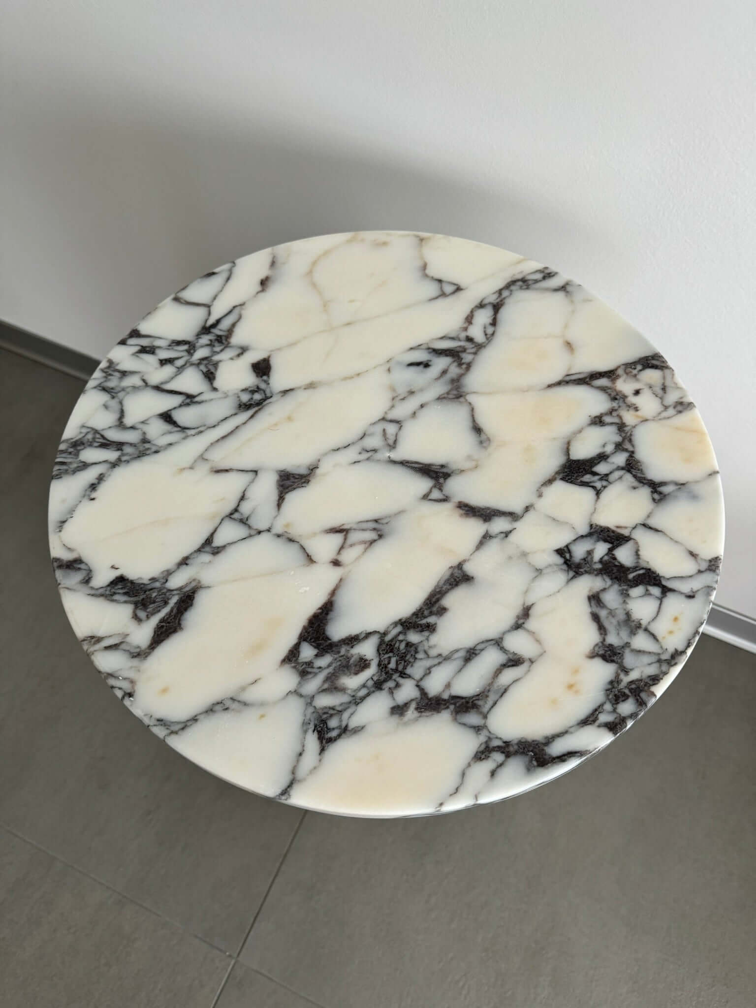 The Ela Prestige Calacatta Viola Marble Coffee Table by Travertable showcases a luxurious, handcrafted marble top with a white background and striking black veining, set against neutral walls and a tile floor.