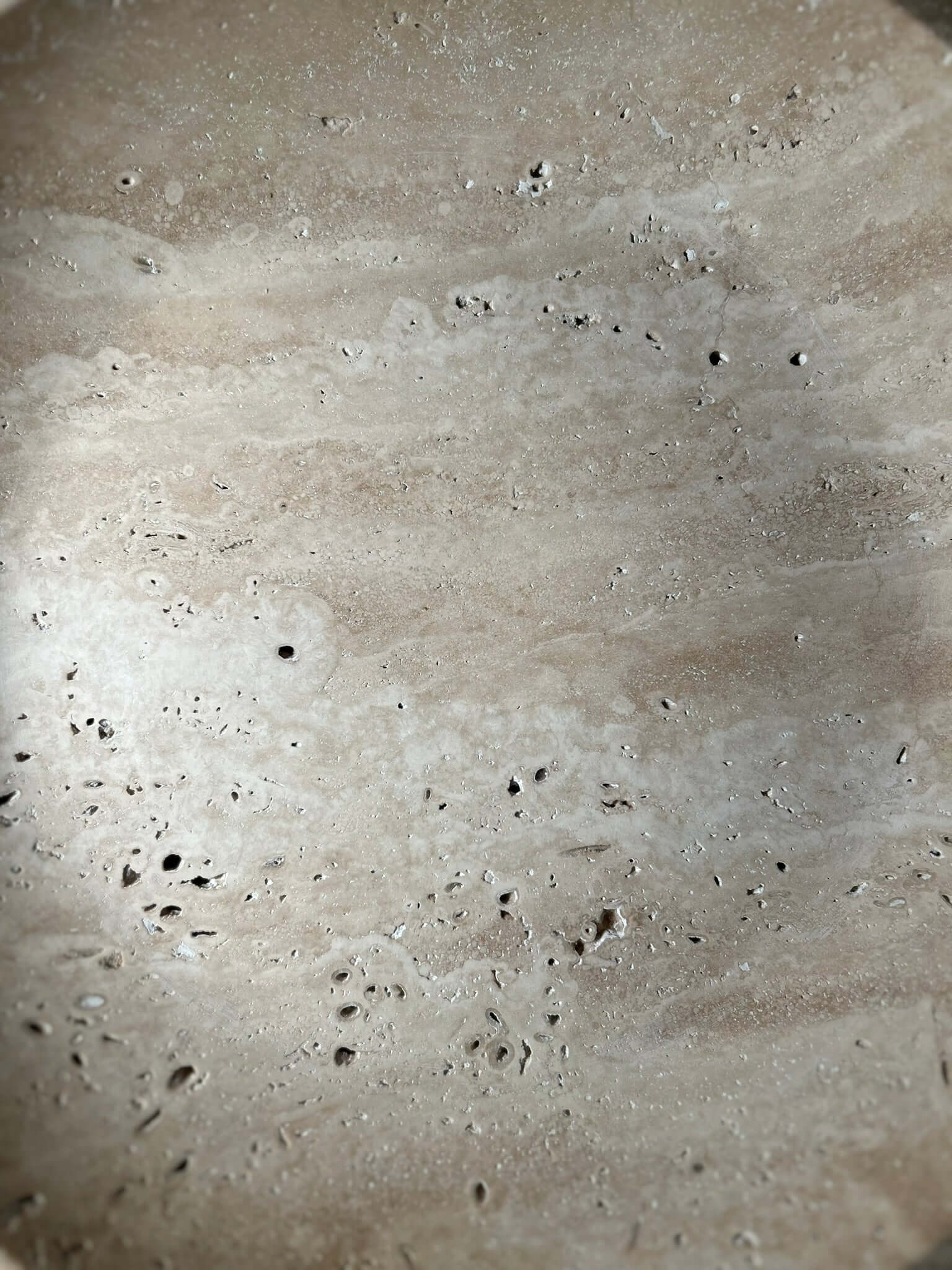 The Timeless Travertine Artisanal Bowl by Travertable features a textured beige surface with scattered small holes and speckles, reminiscent of natural travertine. Its subtle color and texture variations showcase natural artistry, offering an earthy and rustic ambiance.