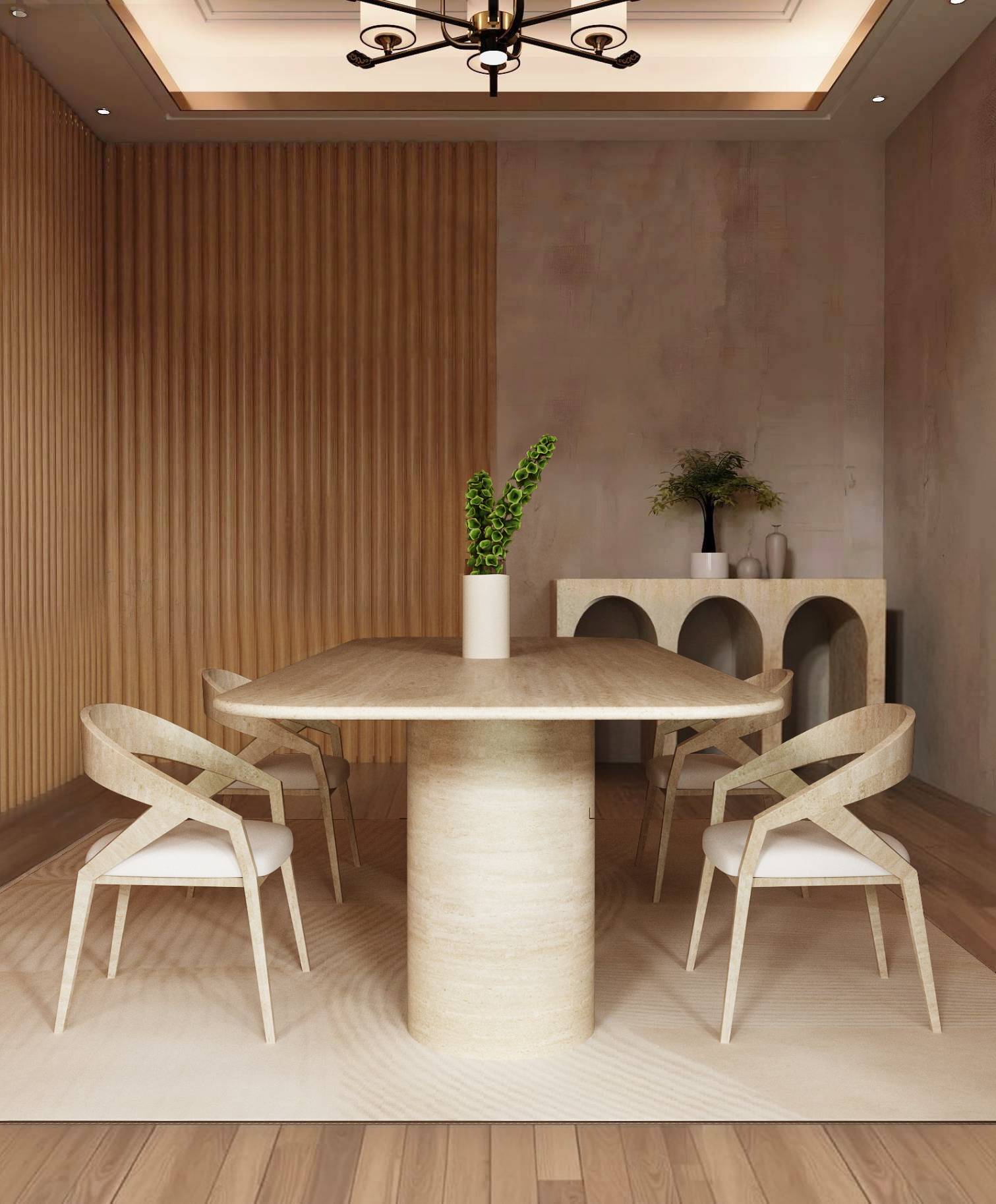 A modern dining room features the TRAVERTABLE Rectangular Travertine Dining Table with a sloped natural stone base, four matching chairs, a cream rug, and a wooden accent wall. A white vase with green stems sits on the table; decor accents the sideboard.