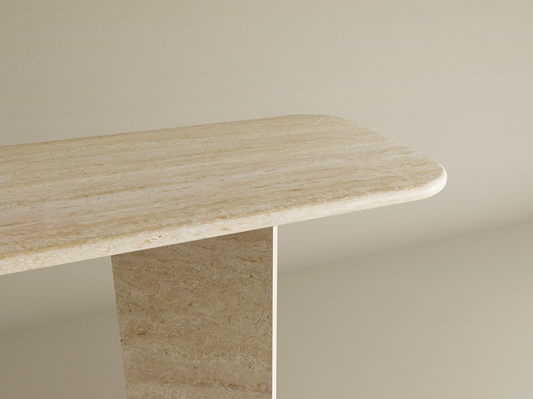 A close-up of the TRAVERTABLE Rectangular Travertine Console Table with Split-V Stone Pedestal Base highlights its modern silhouette and light travertine finish against a plain beige background. Customizable design available.