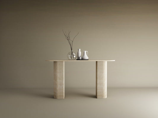 The TRAVERTABLE Ovale Travertine Console Table features a solid, fluted round base and natural stone texture. Against a beige backdrop, three minimalist vases—one with bare branches—adorn its surface in a modern, understated style.
