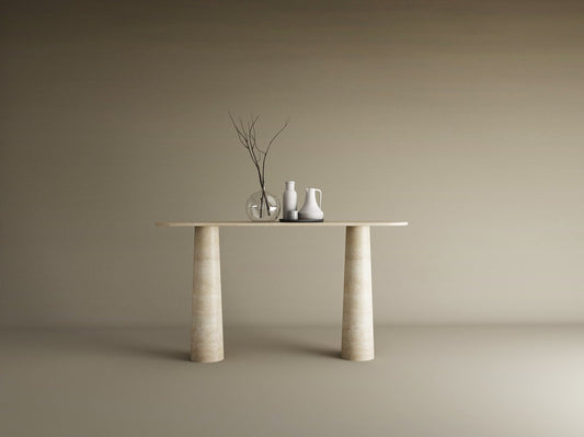 The Ovale Travertine Console Table by TRAVERTABLE features an organic travertine stone top and conical pedestal base. Three ceramic vases—one transparent, two opaque—with bare branches sit against a plain beige background.