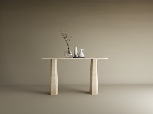 The TRAVERTABLE Rectangular Travertine Console Table with a solid, tapered round base displays a glass vase and ceramic vessels in minimalist beige, set against a plain background. This customizable piece offers contemporary elegance.