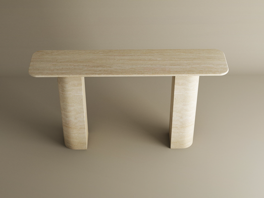 The TRAVERTABLE Rectangular Travertine Console Table features a customizable natural stone top and a sloped pedestal base, offering a minimalist sculptural design perfect against a plain beige background.