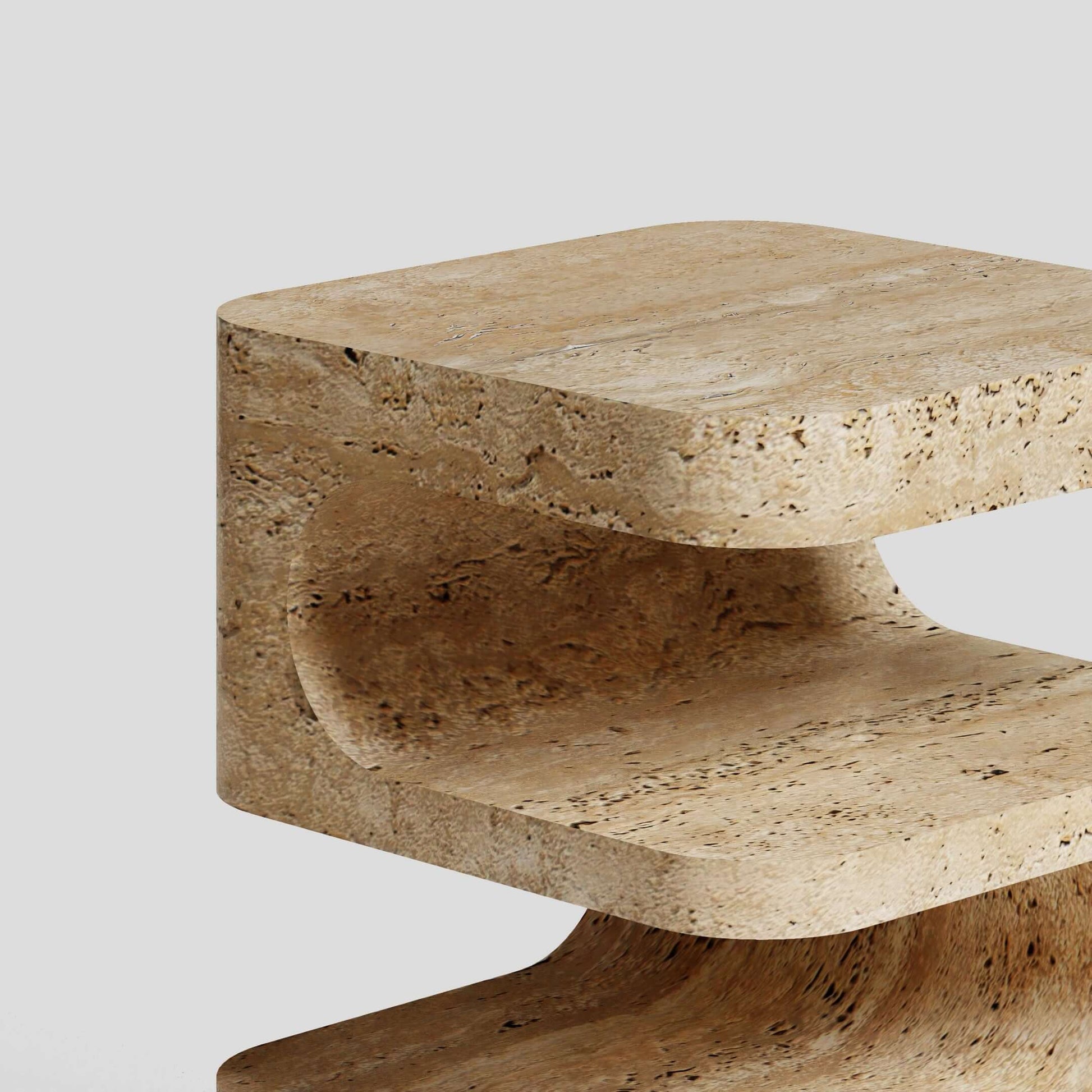 A close-up of the Serenity Block Travertine Table by Travertable reveals its C-shaped design with smooth, rounded edges and a natural stone texture against a plain light gray background. This elegant table melds functionality with timeless style.