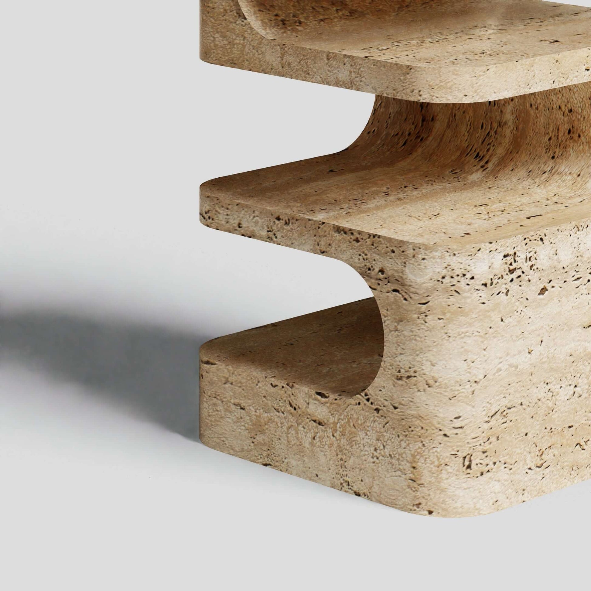 Close-up of Travertables Serenity Block Travertine Table, showcasing smooth curves and a natural texture against a gray background. The light casts a subtle shadow, highlighting its unique patterns and earthy tones.