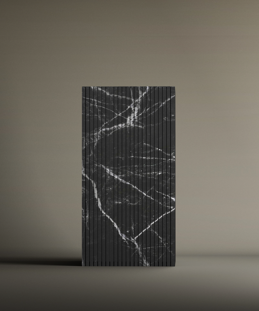 The TRAVERTABLE Nero Marquina Square Fluted Marble Pedestal Vanity Sink is a rectangular, upright sink with vertical grooves and a black surface featuring irregular white marble-like veins, set against a plain beige background.