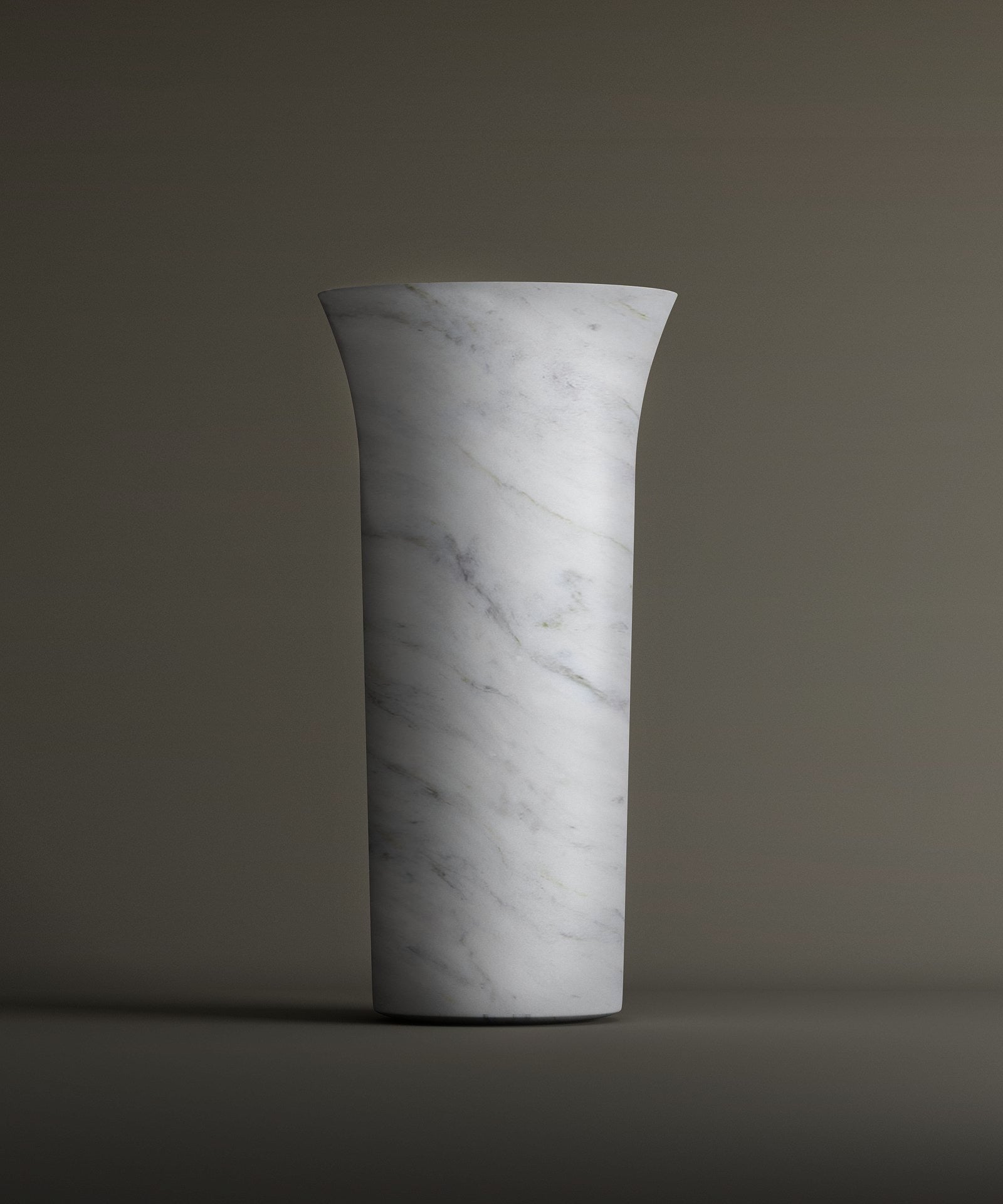 The TRAVERTABLE Carrara Marble Cylinder Pedestal Vanity Sink, with a tall cylindrical shape, white marble finish, and subtle gray veining, stands upright against a plain background. It features a slightly flared rim for added elegance.